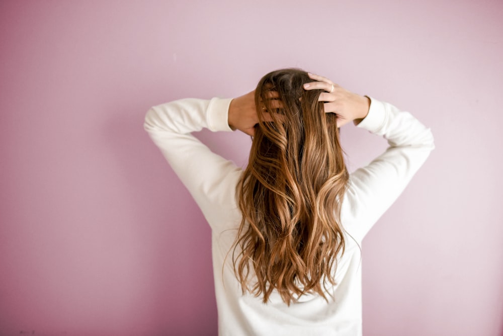 A person flipping healthy, wavy hair against a pink background