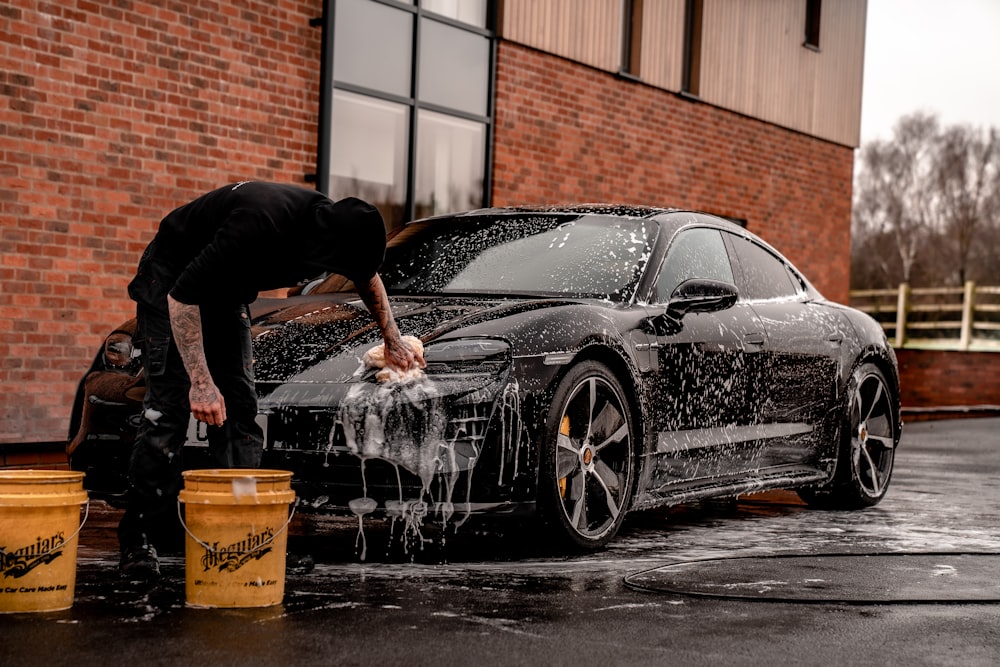 A person hand-washing a car with soap and buckets